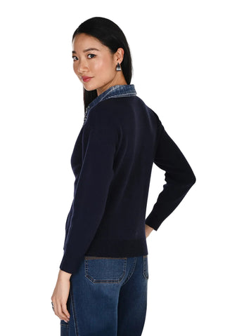 Woman wearing a navy sweater over a denim shirt with a white background