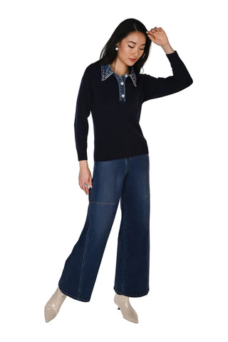 A woman modeling a long-sleeve navy knit polo-style top with a contrasting patterned collar, paired with dark blue wide-leg jeans and beige pointed-toe heels, against a plain white studio background.