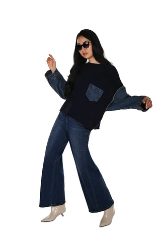 A woman modeling a dark navy long-sleeve top with contrasting medium-wash denim sleeves and a matching denim chest pocket, paired with dark blue wide-leg jeans and beige pointed-toe heels, against a plain white studio background.