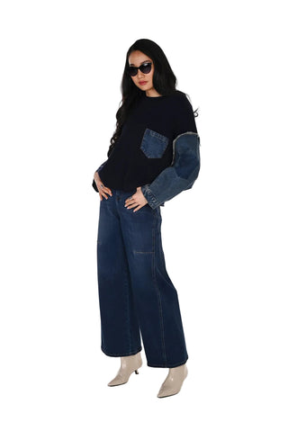 A woman modeling a dark navy long-sleeve top with contrasting medium-wash denim sleeves and a chest pocket, paired with dark blue wide-leg jeans and beige pointed-toe heels, against a plain white studio background.