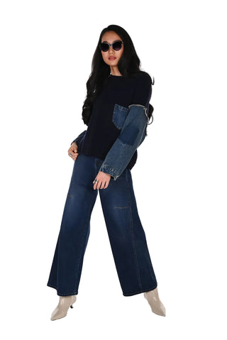 Woman wearing a dark sweater with patchwork design and wide-leg jeans on a white background