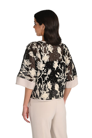 Woman wearing a black floral patterned top with white accents on a plain background