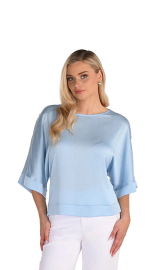 Woman wearing a light blue top with a plain background, featuring the brand 'Frank Lyman Montréal'.