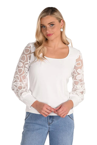 Woman wearing a white long-sleeve top with sheer heart patterns and blue jeans on a white background