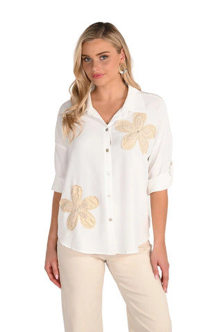 Woman wearing a white blouse with floral designs on a plain background