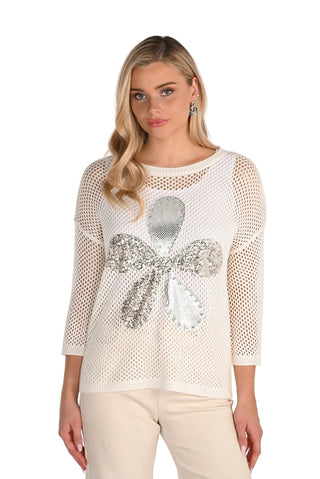 Woman wearing a white mesh top with a decorative bow on a plain background