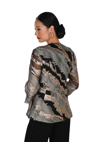 A woman shown from the back wearing a sheer long-sleeve blouse with a metallic abstract pattern in silver, bronze, and black, paired with black pants, against a plain white background.