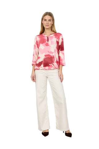 Woman wearing pink and cream print top with cream pants on a white background.