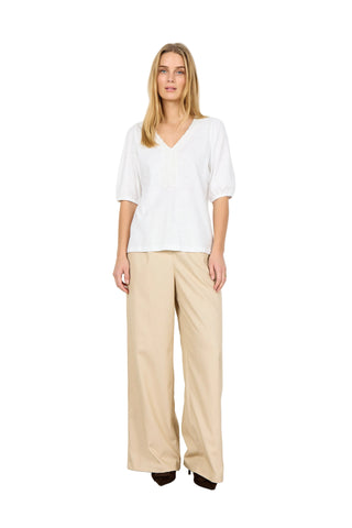 Woman wearing a white top and beige pants against a white background