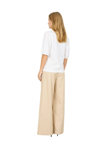 Woman wearing a white top and beige pants against a white background