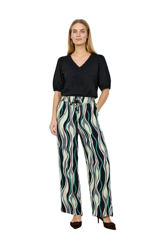 Woman wearing a black top and patterned pants against a white background