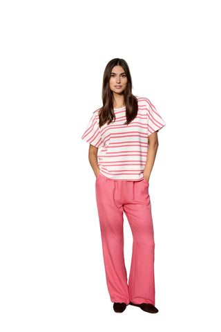 Woman wearing a striped shirt and pink pants against a white curtain background