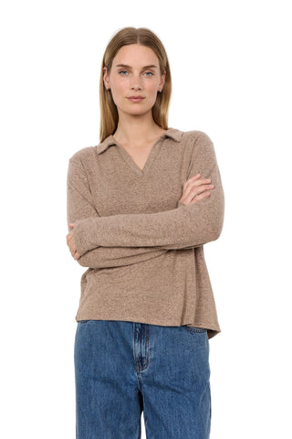 A woman modeling a light brown knit polo sweater with a V-neck and collar, paired with blue jeans, against a plain white studio background.