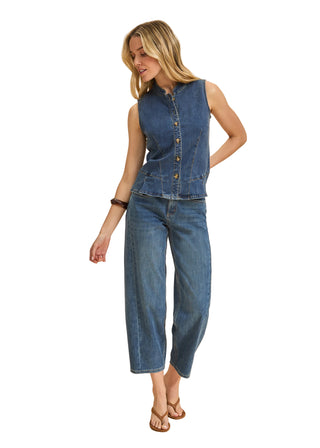 Woman wearing a denim vest and jeans on a beige background