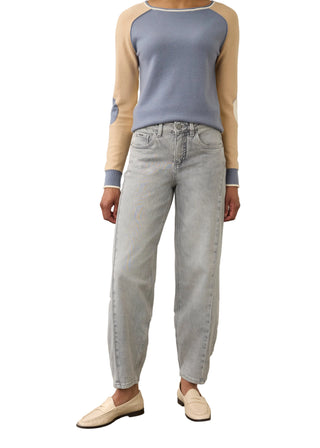 A model wearing a light blue-gray knit sweater with beige raglan sleeves, paired with light-wash straight-leg jeans and cream loafers, standing against a neutral studio background.