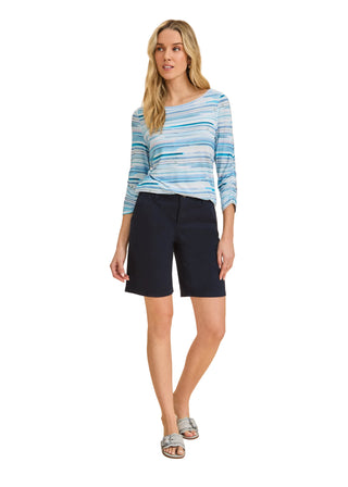 Woman wearing a blue striped shirt and navy shorts on a beige background