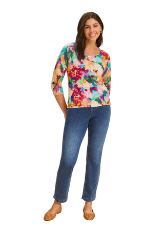 Woman wearing a colorful floral top and blue jeans on a beige background