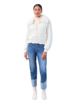 Woman wearing a white sweater, blue jeans, and white shoes against a plain background