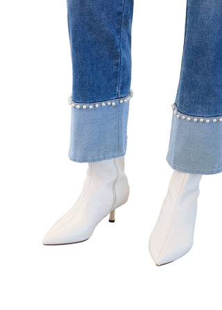 White pointed-toe boots worn with blue jeans featuring pearl details on a neutral background