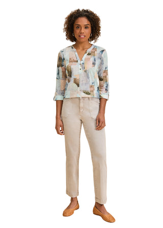 Woman wearing a patterned blouse and beige pants on a beige background