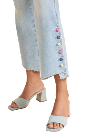Light blue denim skirt with colorful buttons worn by a person, paired with light blue sandals on a beige background.
