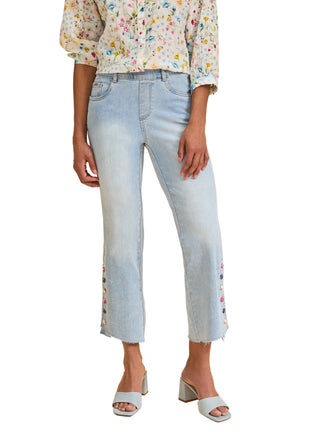 Person wearing light blue jeans with floral top on a beige background