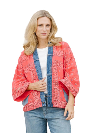 Woman wearing a red lace kimono over a denim jacket against a beige wall.
