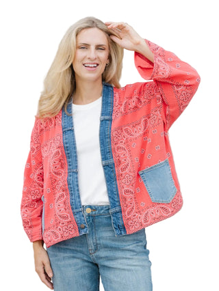 Woman wearing a red bandana print jacket over a denim jacket and jeans against a beige wall.
