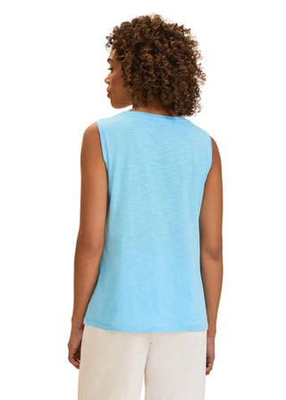 Woman wearing a light blue sleeveless top against a beige background