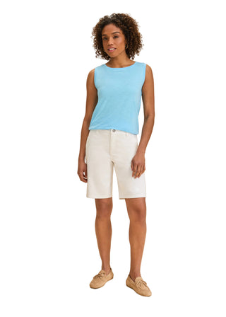 Woman wearing a light blue sleeveless top and white shorts on a beige background