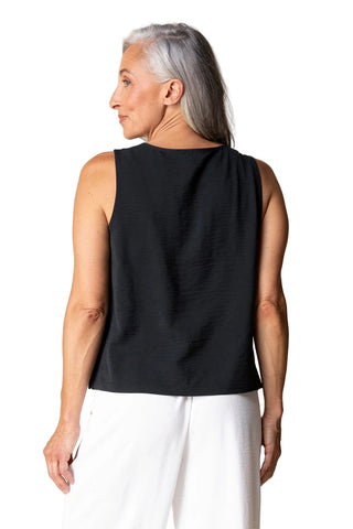 Woman wearing a black sleeveless top and white pants against a beige background