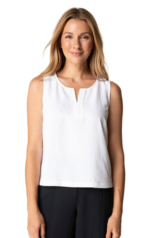 Woman wearing a white sleeveless top and black pants against a beige background