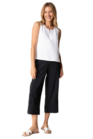 Woman wearing a white sleeveless top and black pants against a beige background