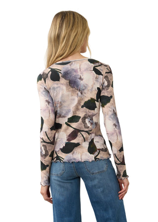A woman viewed from the back wearing a long-sleeve floral top with a beige, gray, and black watercolor-style print, paired with blue jeans, against a plain light background.