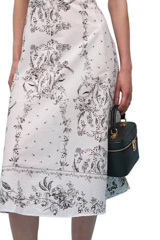 Person wearing a white dress with black floral pattern holding a black handbag against a light blue background