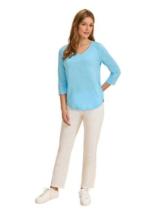 Woman wearing a light blue sweater and white pants on a beige background