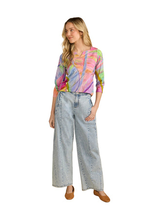 Woman wearing a colorful blouse and light blue jeans against a beige background