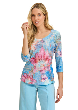 Woman wearing a colorful floral top and light blue pants on a beige background