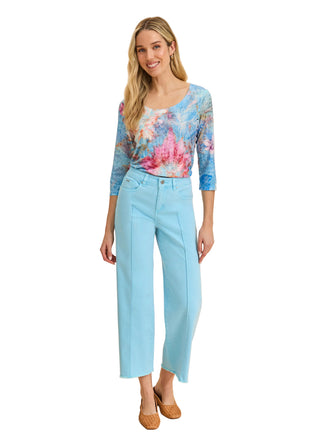 Woman wearing a colorful top and light blue pants on a beige background