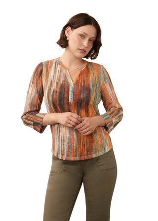 A woman modeling a long-sleeve V-neck blouse with a vertical striped pattern in orange, blue, and beige, paired with olive green pants, against a plain light gray background.
