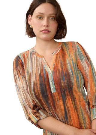 A woman wearing a lightweight, semi-sheer long-sleeve top with a vertical multicolor stripe pattern in orange, blue, beige, and brown, featuring a split neckline with three buttons.