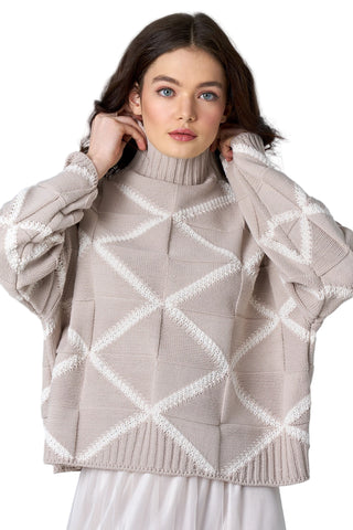 Woman wearing a beige sweater with white geometric patterns on a light gray background