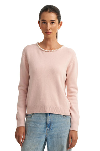 Woman wearing a light pink sweater and blue jeans against a white background