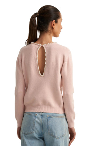Woman wearing a light pink sweater with a unique back design on a white background