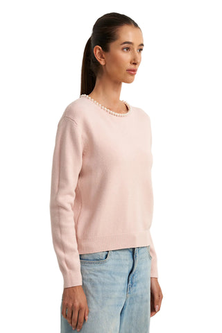 Woman wearing a pink sweater with pearl details against a white background