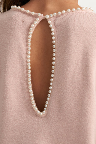 Close-up of a pale pink knit top with a large keyhole cutout at the back, bordered by a row of white faux pearls.