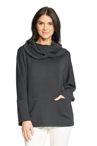 A woman modeling a black long-sleeve cowl-neck top with side pockets, paired with white pants, against a light gray studio background.