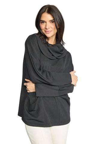 A woman modeling a black draped long-sleeve top with a cowl neckline and side pockets, paired with off-white pants, against a light gray studio background.