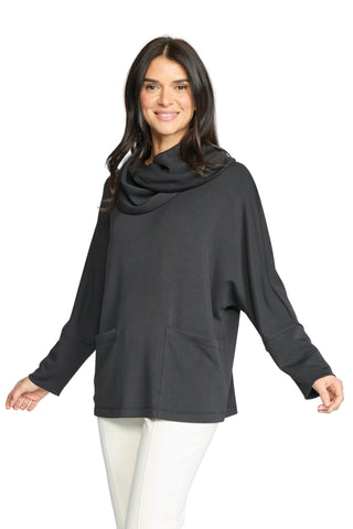 A woman modeling a dark charcoal gray cowl-neck long-sleeve top with front patch pockets, paired with off-white pants, against a light gray studio background.