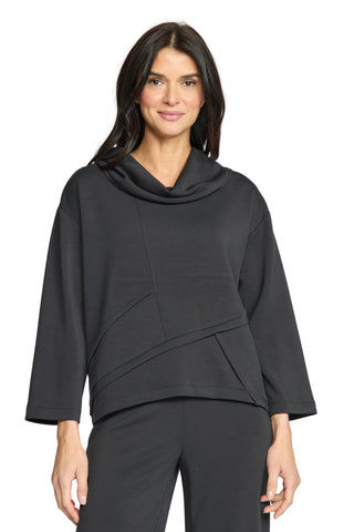 A woman modeling a black cowl-neck long-sleeve top with draped panel details, paired with black pants, against a light gray studio background.